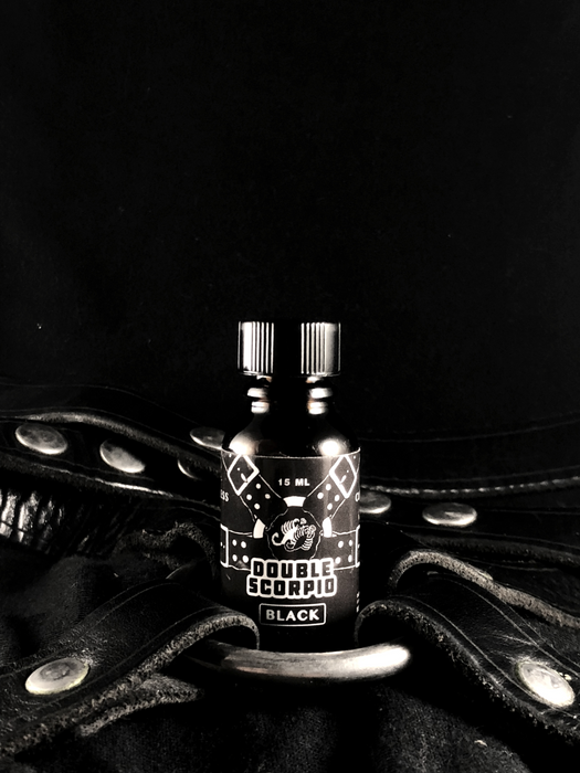 Botella de aroma Double Scorpio Black sobre un arnés strap on de cuero